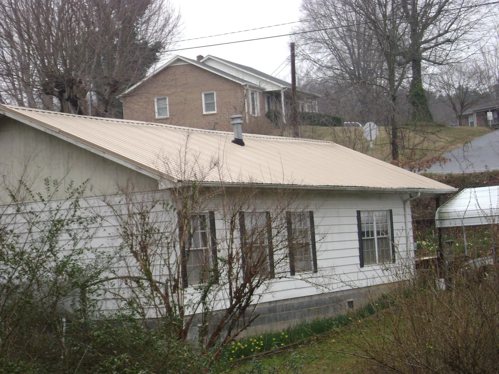 Tan metal roof on a white sided house set into a hillside — Commercial Roofing by Roofing Brothers in Manning